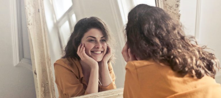 woman smiling in the mirror after doing skincare routine